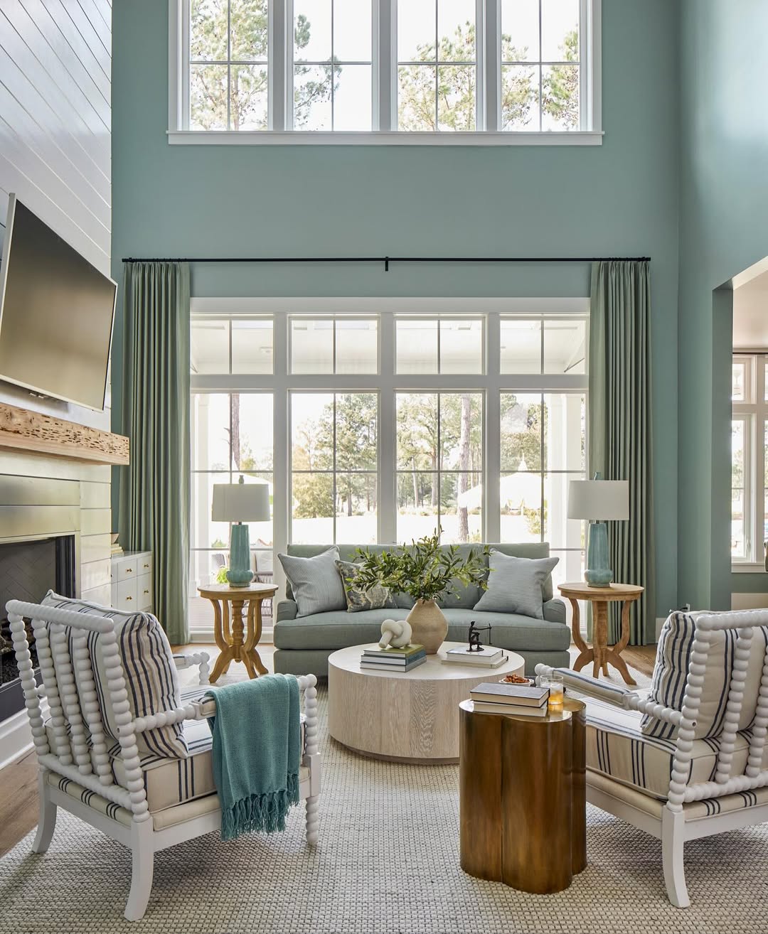 A bright living room with tall windows, light blue walls, a sofa, armchairs, round coffee table, fireplace, and decorative accents—perfect inspiration for Living Room Ideas featured in any design magazine.