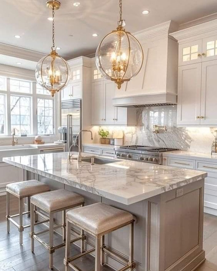 Modern kitchen with white cabinets, a marble island countertop, three upholstered stools, stainless steel appliances, and two globe pendant lights—showcasing one of the top kitchen trends 2025 for stunning kitchen colors and timeless style.