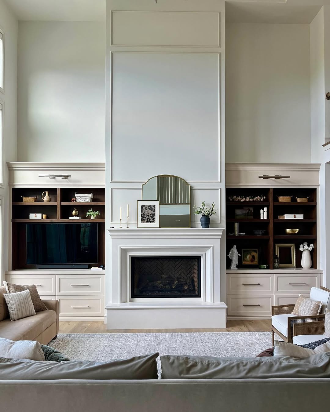 A modern built-in shelves living room features a cozy fireplace, stylish decor, a TV on the left, neutral-toned furniture, and a spacious rug.
