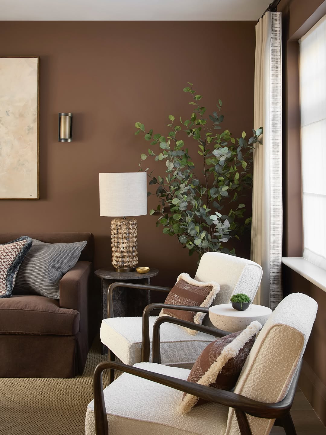 A chic living room featuring dark brown sofas, two white armchairs, a floor plant, a lamp on a side table, and a large window with white curtains—perfect for modern living room ideas.