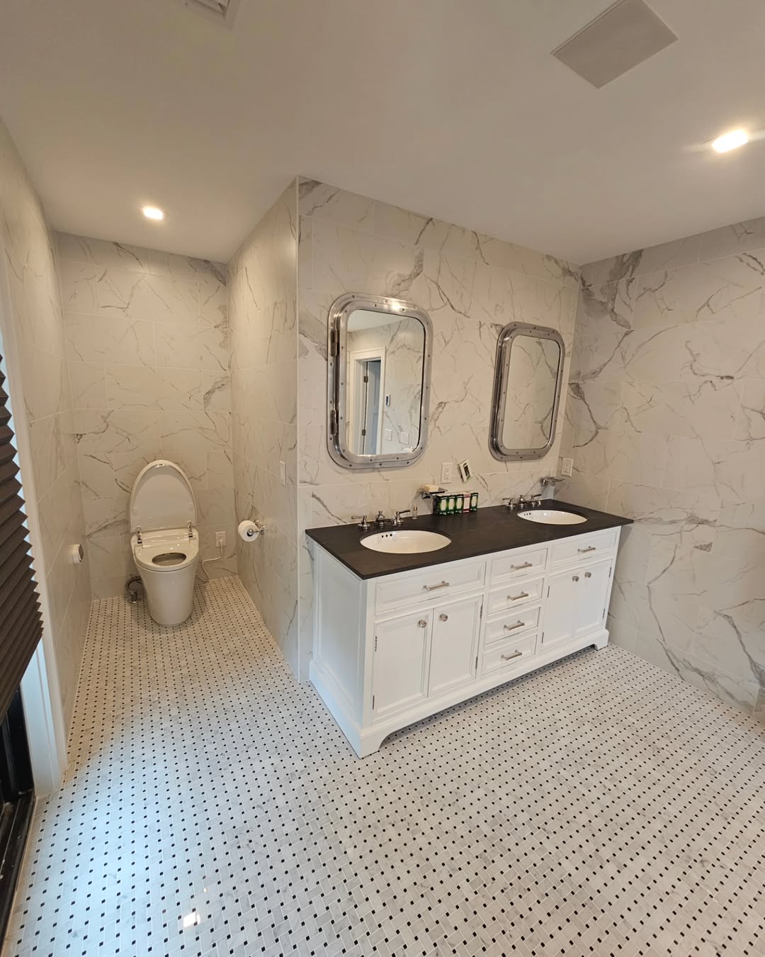 Modern bathroom with marble walls, double sink vanity with two mirrors, and a separate toilet area; black and white patterned floor tiles showcase inspiring bathroom tile ideas for a spa-worthy bathroom design.