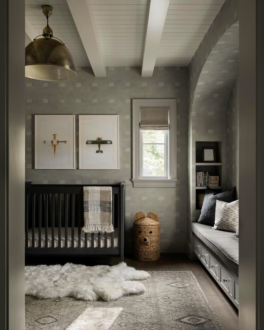 A cozy baby boy nursery featuring a black crib, airplane prints, a Roman shade, furry rug, woven bear basket, and built-in daybed with storage—perfect for first-time moms seeking the latest nursery ideas 2025.