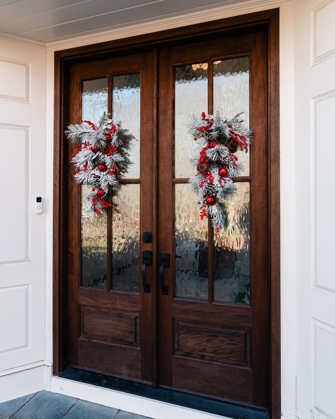 Double wooden doors with frosted glass panes make a stunning double door entryway, adorned with festive wreaths of frosted greenery and red berries.