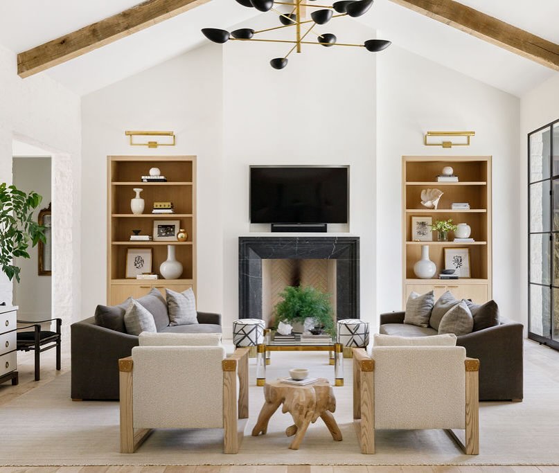 Modern living room with vaulted ceiling, black chandelier, fireplace, TV, two armchairs, two sofas, wooden shelves, and a small wooden table in the center—perfect for those seeking organic modern living room ideas.