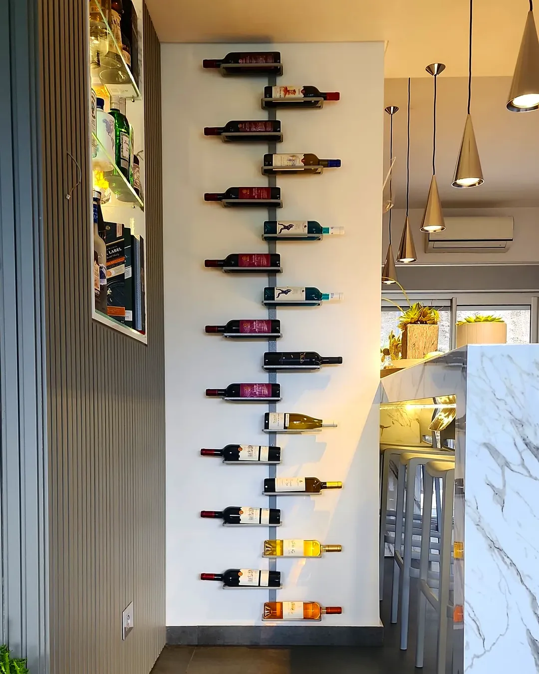 Wall-mounted wine rack offers stylish wine storage, holding several bottles vertically in a modern kitchen with pendant lights and a marble counter.