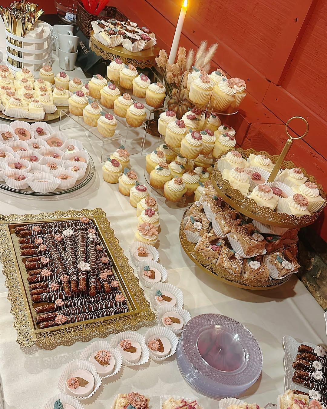 A dessert table filled with assorted cupcakes, pastries, and cookies arranged on trays and tiered stands—perfect inspiration for party desserts—with a lit candle and cups in the background.