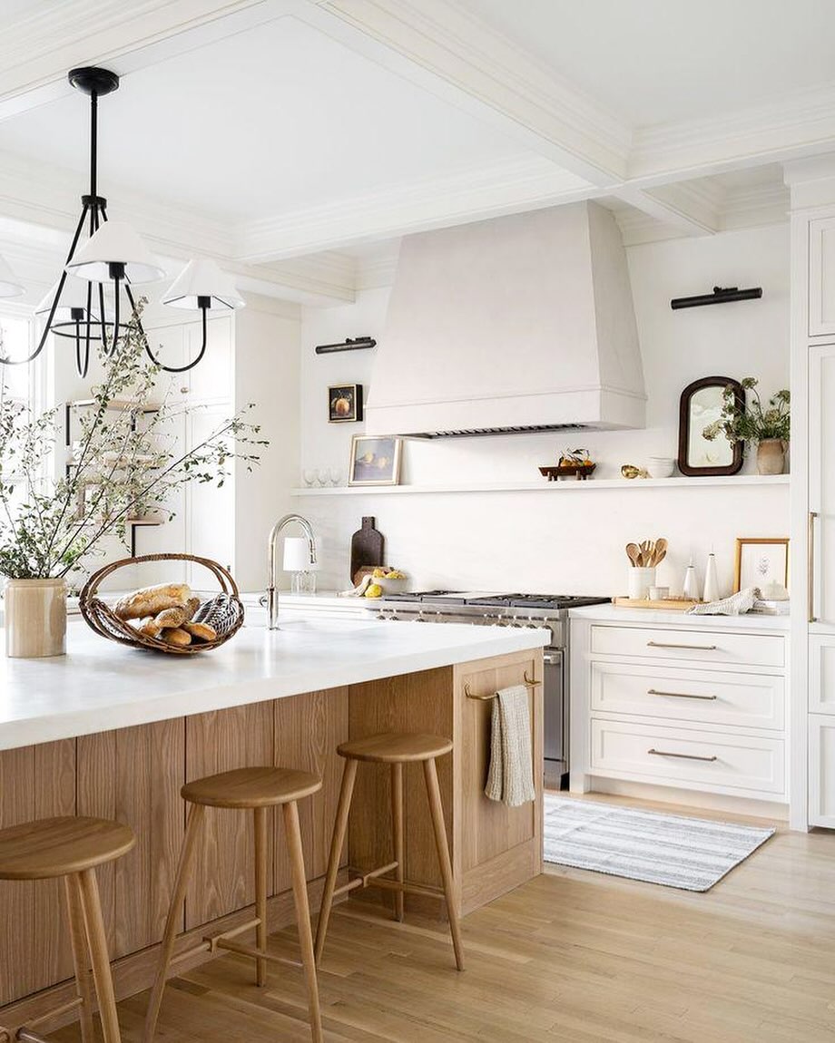 Bright, modern kitchen with white cabinets, wooden stools, a marble island, and decorative plants. Discover stunning kitchen colors for inspiration—perfect if you
