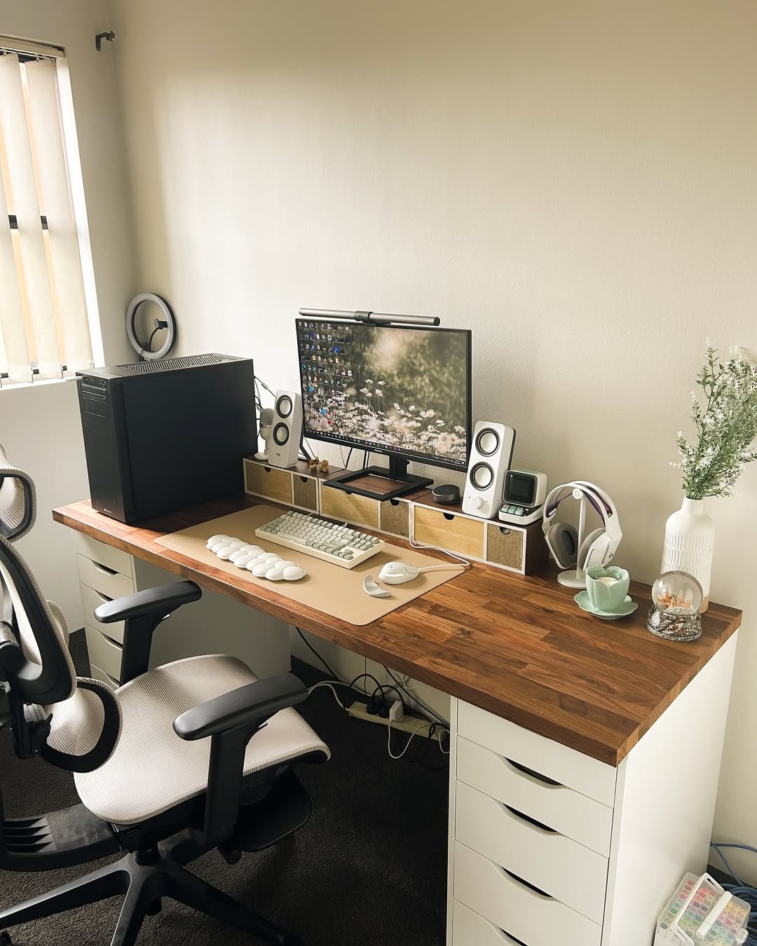 A tidy home office setup showcases smart computer desk design, featuring a computer, monitor, speakers, keyboard, and mouse on a wooden desk, complemented by a chair, headphones, cup, and a vase with flowers.