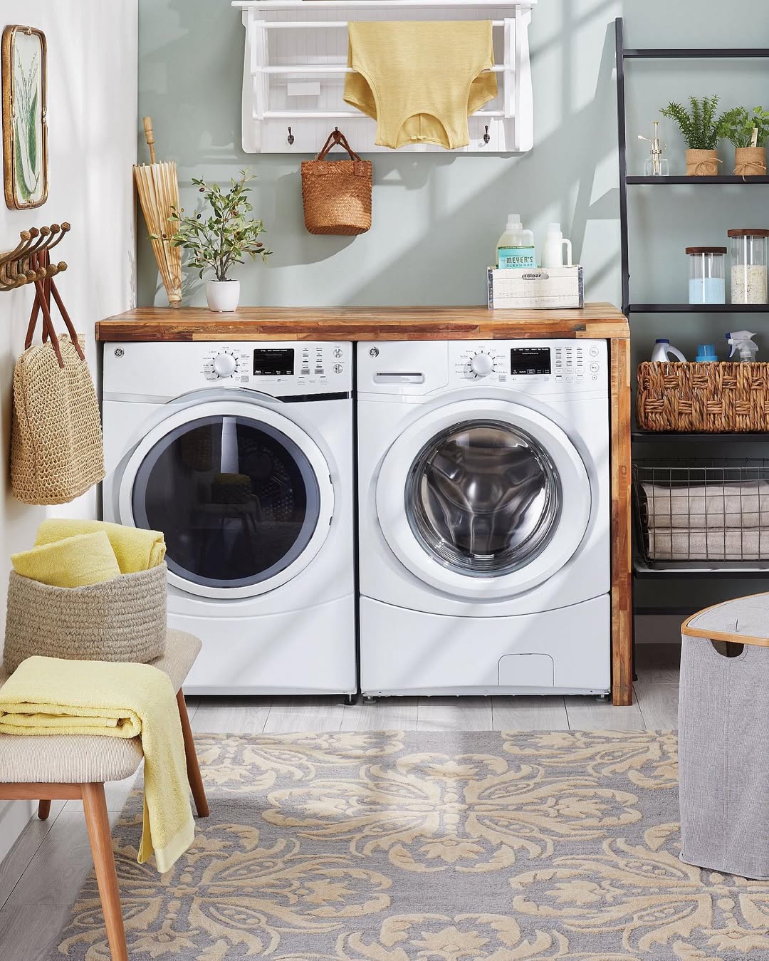 A laundry room with a washing machine and dryer side by side, wooden countertop, shelves with baskets and cleaning supplies, plus yellow and beige accents—perfect for those seeking boho laundry room ideas.